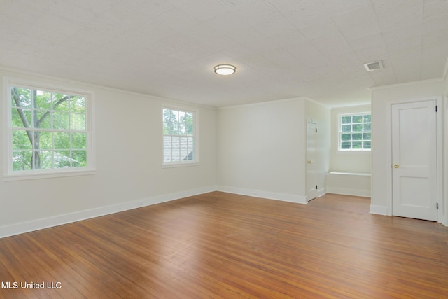 empty room with a wealth of natural light, visible vents, and wood finished floors