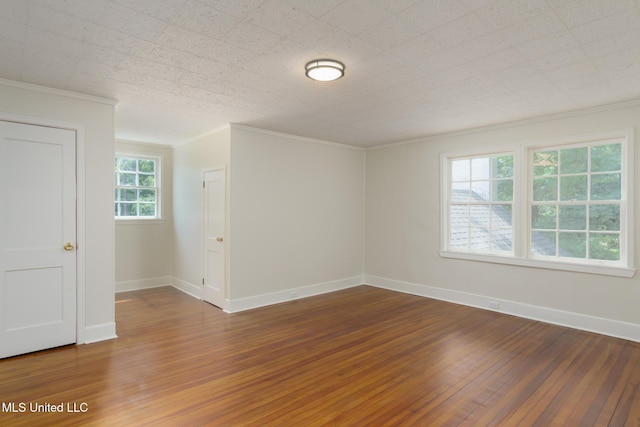 spare room featuring baseboards, wood-type flooring, and crown molding