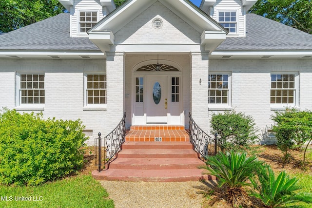 doorway to property with brick siding and roof with shingles