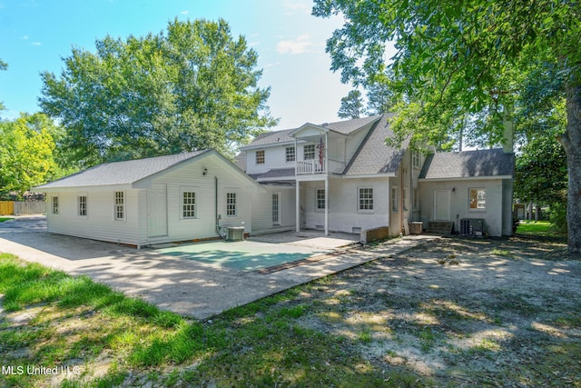 rear view of property with central AC unit, a patio area, a balcony, and a shingled roof