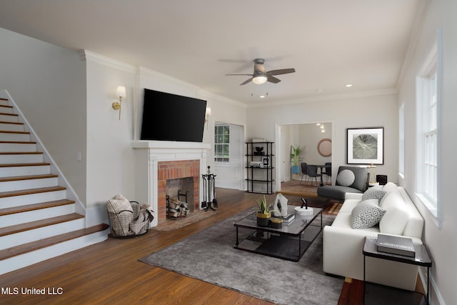 living area featuring ornamental molding, a brick fireplace, wood finished floors, baseboards, and stairs