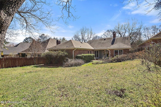 back of property featuring brick siding, fence, a chimney, and a lawn