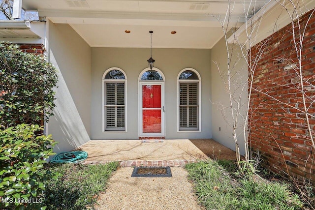 entrance to property featuring a patio area, brick siding, and stucco siding