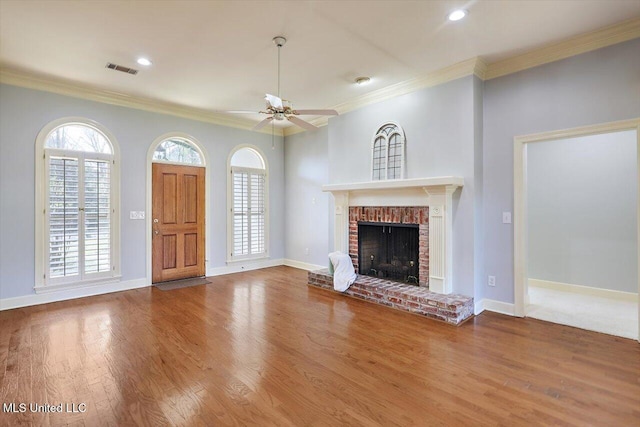 unfurnished living room featuring plenty of natural light, visible vents, ornamental molding, wood finished floors, and a brick fireplace