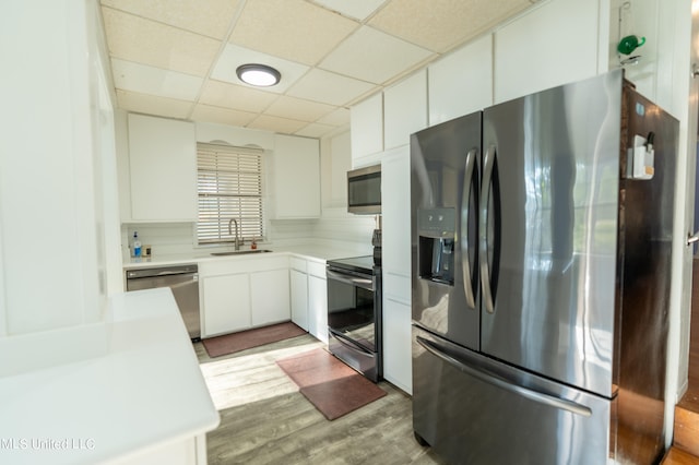 kitchen with a drop ceiling, sink, appliances with stainless steel finishes, white cabinets, and light wood-type flooring