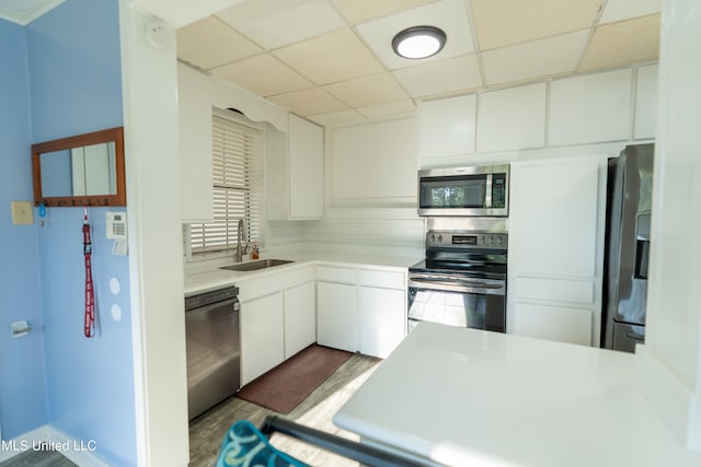 kitchen featuring sink, a drop ceiling, decorative backsplash, white cabinets, and appliances with stainless steel finishes