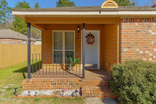 property entrance featuring a porch, fence, and brick siding