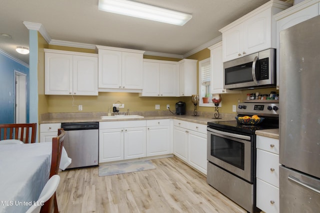 kitchen with stainless steel appliances, light countertops, ornamental molding, white cabinets, and a sink