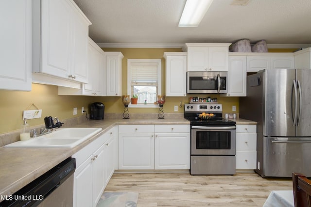 kitchen with stainless steel appliances, a sink, white cabinetry, light wood finished floors, and crown molding