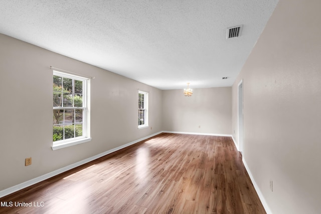 spare room with an inviting chandelier, visible vents, baseboards, a textured ceiling, and wood finished floors