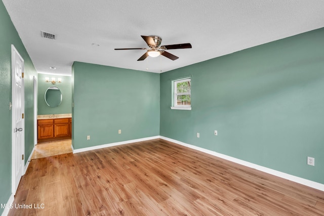unfurnished bedroom with wood finished floors, visible vents, connected bathroom, and baseboards