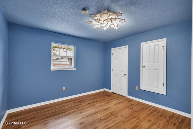 unfurnished bedroom featuring baseboards, wood finished floors, and a textured ceiling