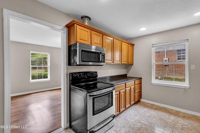 kitchen with appliances with stainless steel finishes, dark countertops, baseboards, recessed lighting, and brown cabinetry