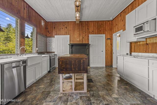 21021 Old River Rd, Vancleave, MS 39565 - kitchen featuring appliances with stainless steel finishes, wood walls, a sink, white cabinetry, and stone finish flooring