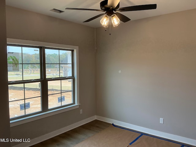 empty room featuring a ceiling fan, visible vents, baseboards, and wood finished floors