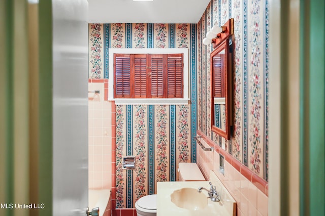 bathroom featuring a bathtub, toilet, tile walls, and sink