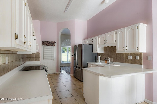 kitchen with arched walkways, a sink, white cabinets, a peninsula, and stainless steel fridge