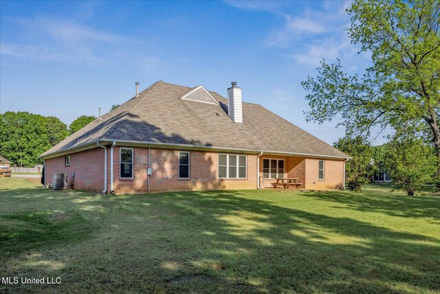 rear view of house featuring cooling unit, a chimney, brick siding, a shingled roof, and a lawn