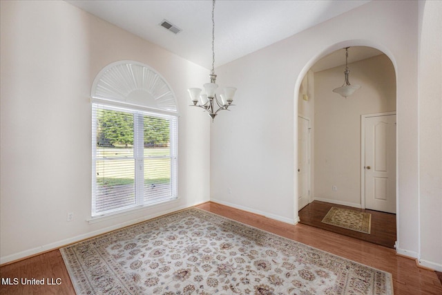 empty room featuring an inviting chandelier, arched walkways, baseboards, wood finished floors, and visible vents