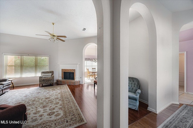 living room featuring arched walkways, ceiling fan, wood finished floors, and visible vents