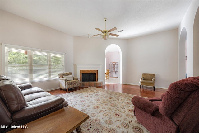 living area featuring arched walkways, ceiling fan, wood finished floors, and a fireplace
