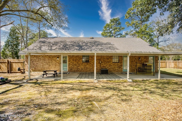 rear view of property featuring brick siding, a shingled roof, a patio, and fence