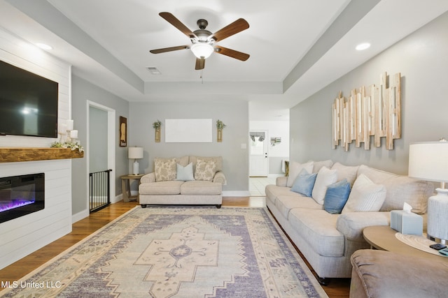 living area featuring a fireplace, a raised ceiling, baseboards, and wood finished floors