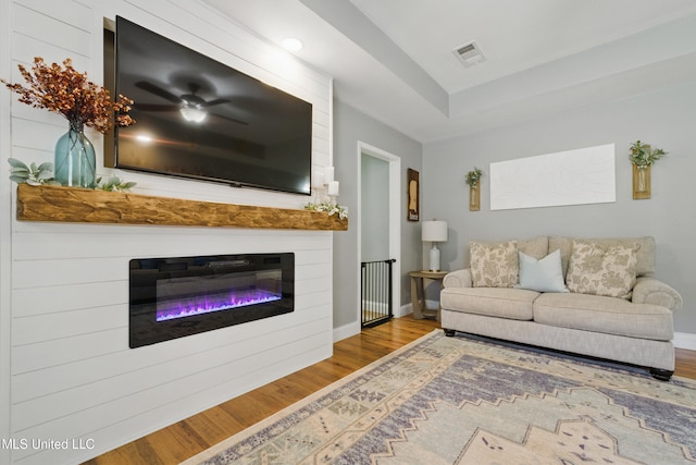 living room with a glass covered fireplace, wood finished floors, visible vents, and baseboards