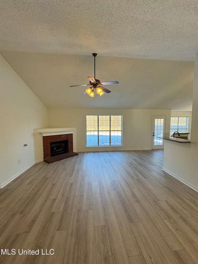 unfurnished living room featuring a fireplace, a textured ceiling, light hardwood / wood-style floors, and ceiling fan