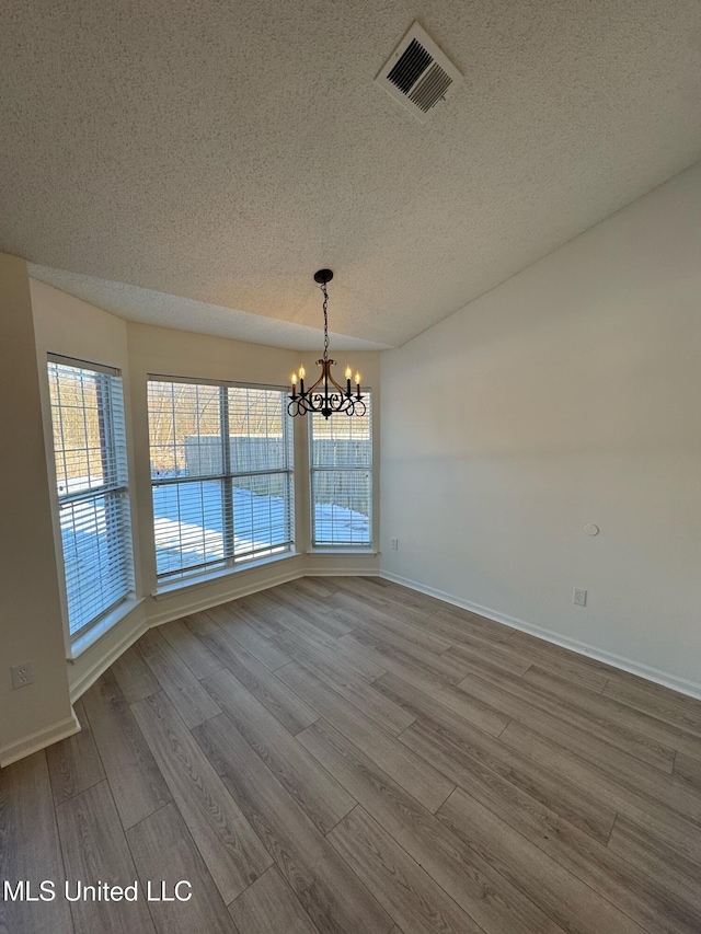 unfurnished dining area with a chandelier, hardwood / wood-style floors, and a textured ceiling