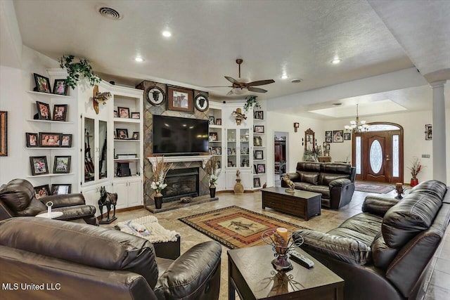 tiled living room featuring decorative columns, ceiling fan with notable chandelier, built in features, and a fireplace