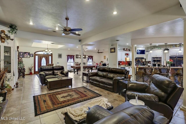 tiled living room with ceiling fan with notable chandelier and a textured ceiling