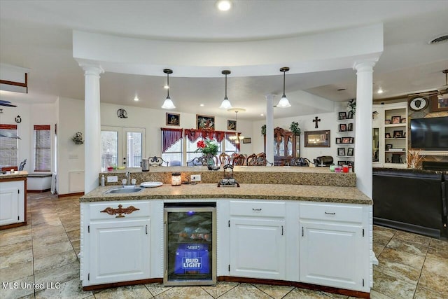 kitchen with ornate columns, sink, white cabinets, beverage cooler, and hanging light fixtures