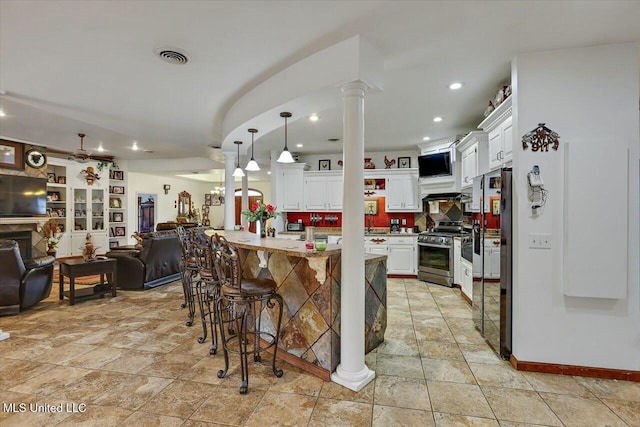 kitchen with a breakfast bar, decorative light fixtures, decorative columns, white cabinetry, and stainless steel appliances