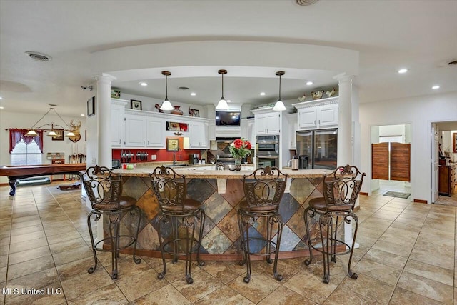 kitchen with stainless steel appliances, white cabinets, a kitchen bar, and decorative light fixtures