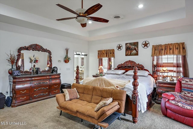 carpeted bedroom with a raised ceiling and ceiling fan