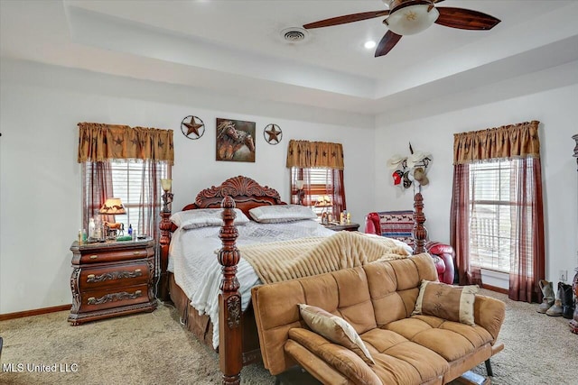 carpeted bedroom with a raised ceiling and ceiling fan