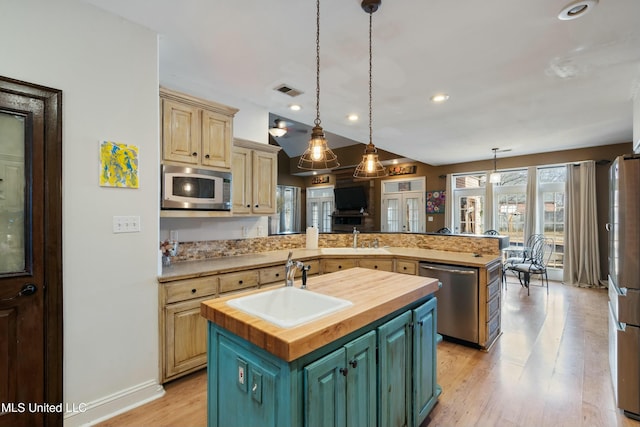 kitchen with wood counters, sink, a center island with sink, pendant lighting, and stainless steel appliances