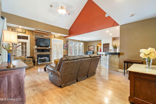 living room featuring a stone fireplace, high vaulted ceiling, and light wood-type flooring