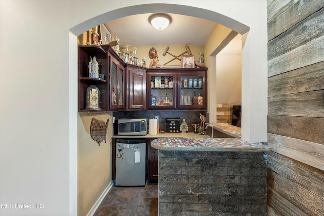 bar with dark brown cabinetry, backsplash, and appliances with stainless steel finishes