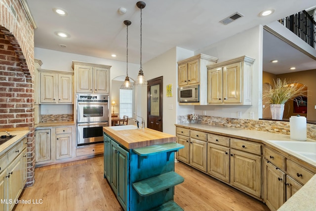 kitchen featuring appliances with stainless steel finishes, butcher block counters, hanging light fixtures, light hardwood / wood-style floors, and a kitchen island