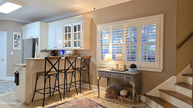 312 Grandview Ct, Pearl, MS 39208 - kitchen with crown molding, a breakfast bar area, glass insert cabinets, white cabinetry, and light stone counters