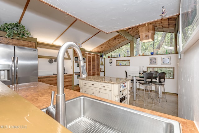 kitchen with white oven, stainless steel fridge, vaulted ceiling, white cabinetry, and light stone counters