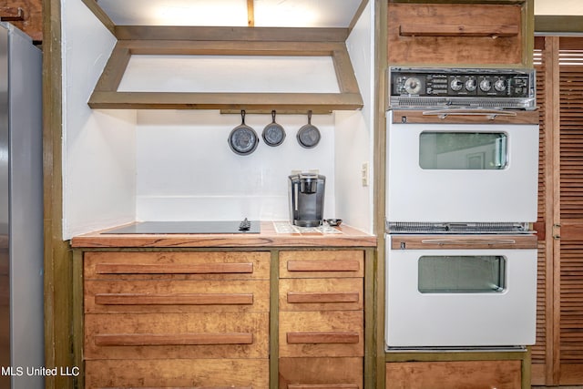 kitchen with black electric stovetop, stainless steel fridge, and white double oven