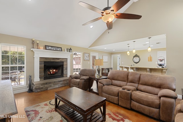 living room featuring light wood-type flooring, a fireplace, ceiling fan, crown molding, and high vaulted ceiling