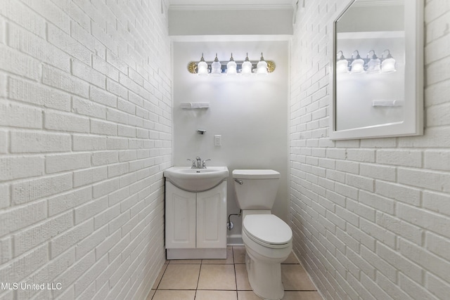 bathroom with brick wall, toilet, vanity, and tile patterned flooring