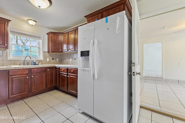 kitchen featuring light tile patterned floors, decorative backsplash, a textured ceiling, white refrigerator with ice dispenser, and sink