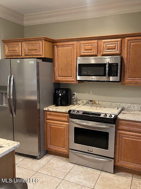 kitchen featuring appliances with stainless steel finishes, ornamental molding, light stone countertops, and light tile patterned floors