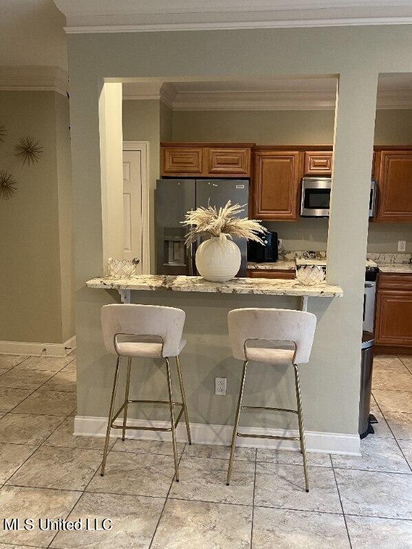 kitchen with refrigerator with ice dispenser, ornamental molding, light stone counters, and a breakfast bar area