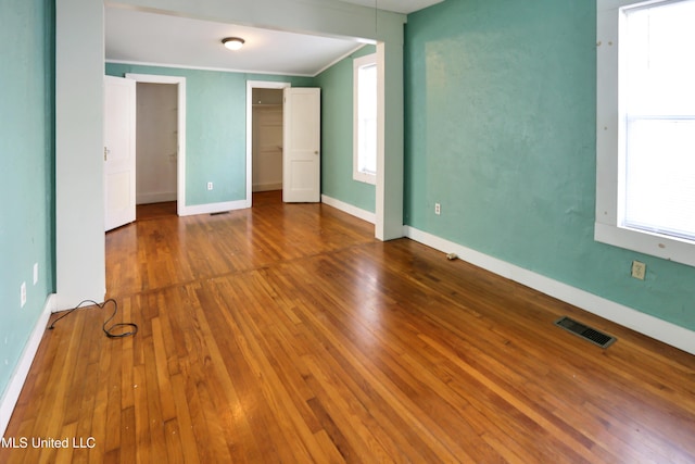 unfurnished bedroom featuring wood-type flooring, a walk in closet, multiple windows, and crown molding